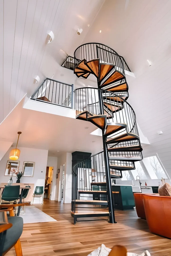 A-frame house interior featuring a spiral staircase with wooden treads, green kitchen cabinetry, mid-century modern dining chairs, and large windows creating a bright atmosphere.