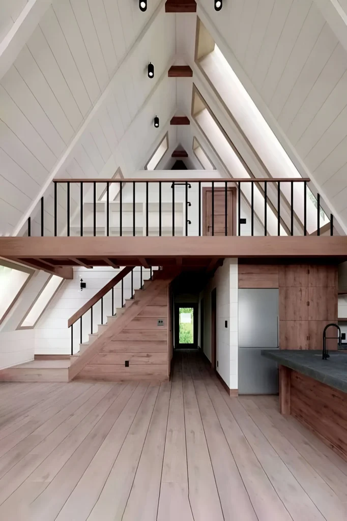 Minimalist A-frame house interior with natural wood finishes, shiplap walls, a light wood staircase, black railing details, and an open loft area.