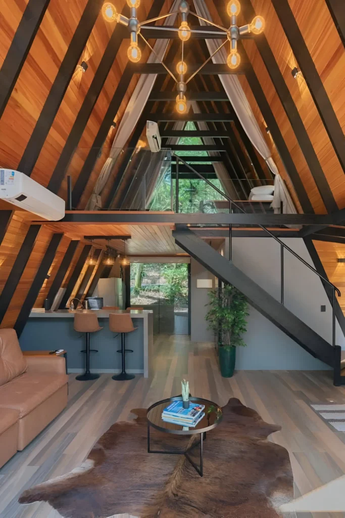 Modern A-frame interior with wood beams, black steel accents, an open loft, stylish kitchen, warm lighting, and a cowhide rug.