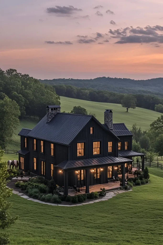 Black farmhouse with glowing windows and a wraparound porch at twilight, surrounded by green hills and a peaceful countryside landscape.