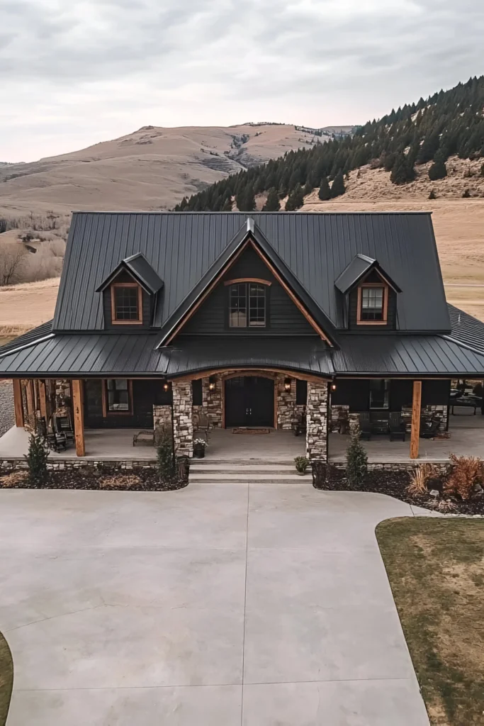 Black farmhouse with a metal roof, stone pillars, and wood accents, surrounded by a wide-open countryside with rolling hills and mountains.