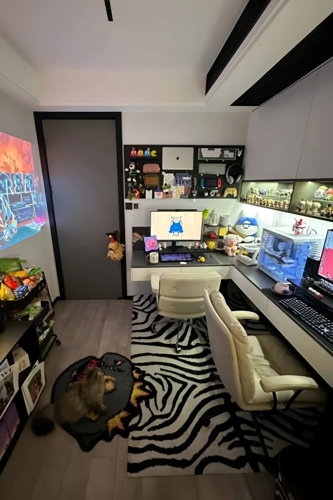 Gaming workspace with dual monitors, collectible figurines, wall-mounted storage, zebra-striped rug, and vibrant decor.