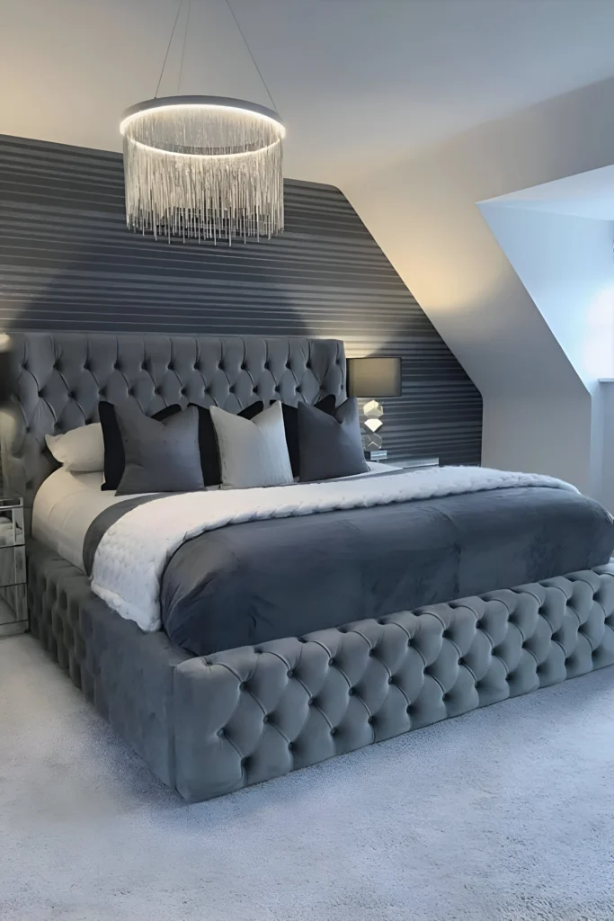 Elegant gray bedroom design featuring a tufted bed, striped accent wall, plush bedding, and a modern chandelier for a sophisticated and cozy ambiance.