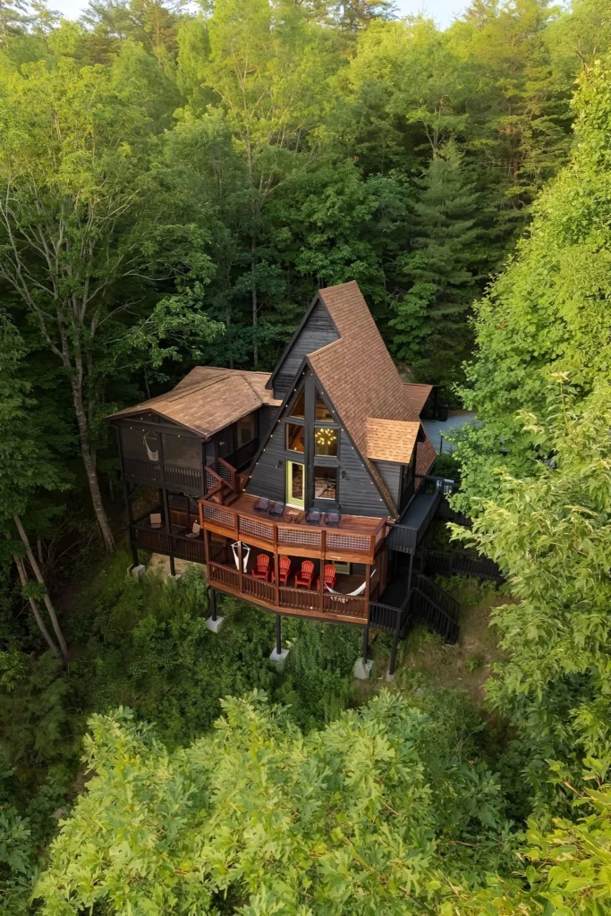 Secluded A-frame house with multi-level wooden decks, cozy seating, and hammocks, surrounded by dense green forest.