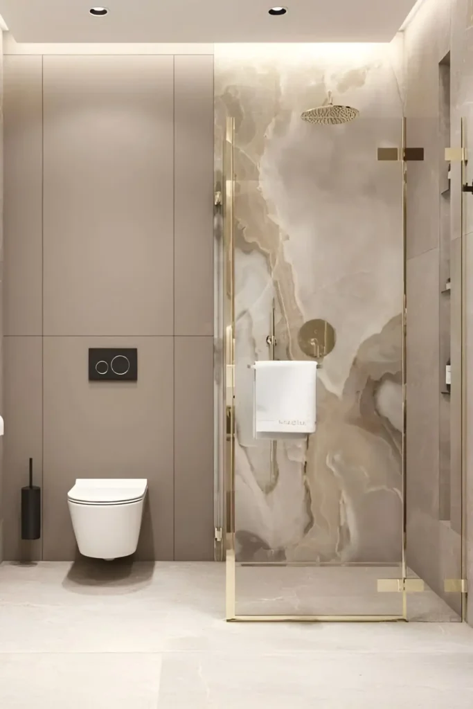 Modern bathroom with beige marble shower, gold accents, wall-mounted toilet, and glass-enclosed shower design.