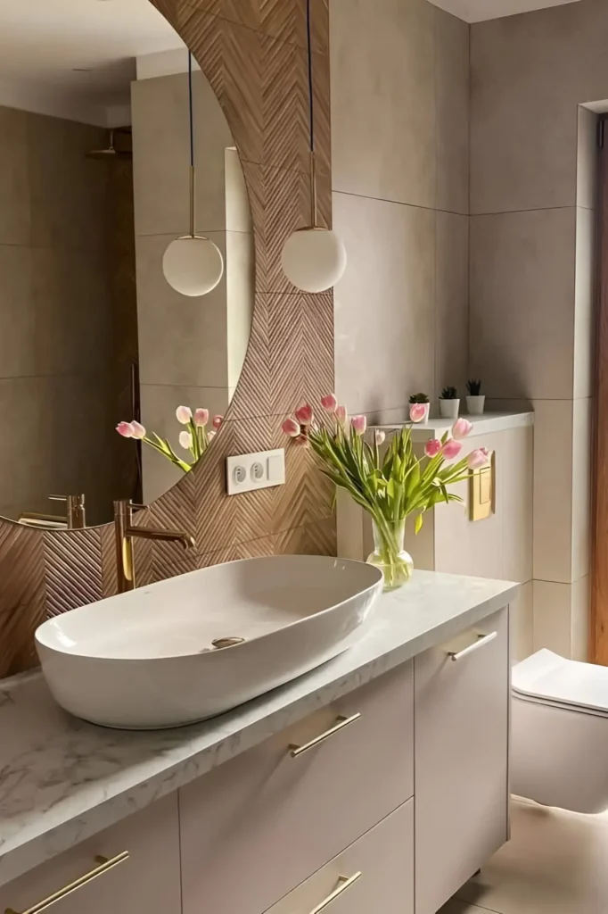 Modern bathroom with marble countertop, vessel sink, gold fixtures, herringbone accent wall, and fresh tulips for a natural touch.
