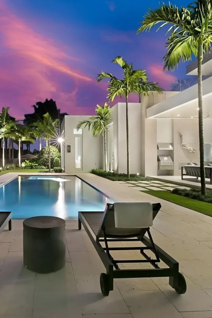 Modern tropical home with a minimalist pool, palm trees, and open-air lounge area under a vibrant sunset.