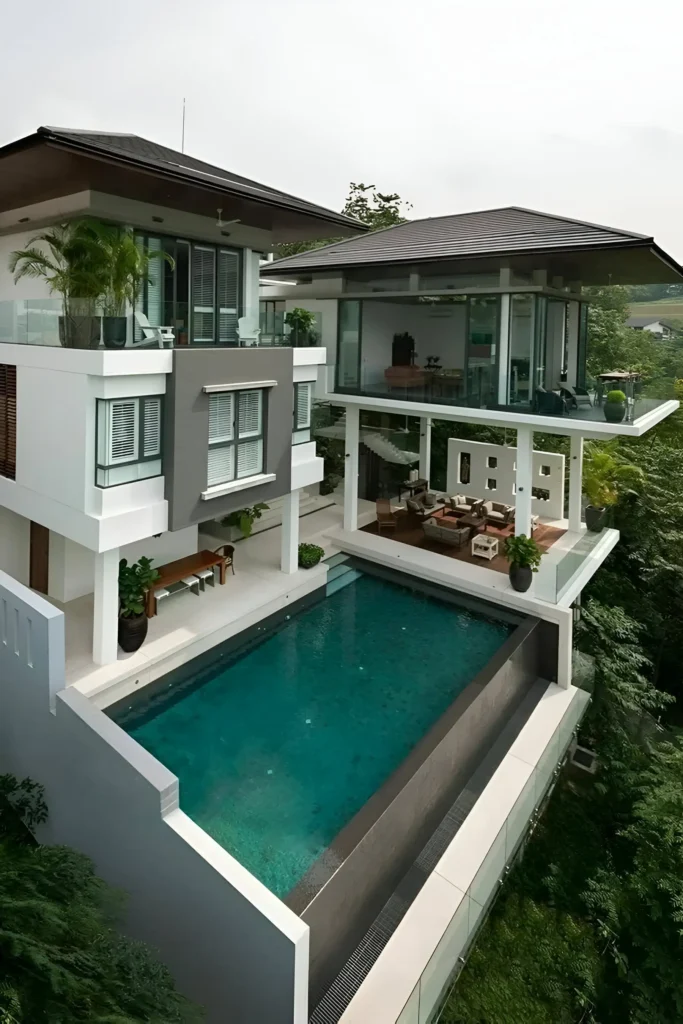 Hillside modern home with an elevated infinity pool, glass walls, and lush greenery surroundings.