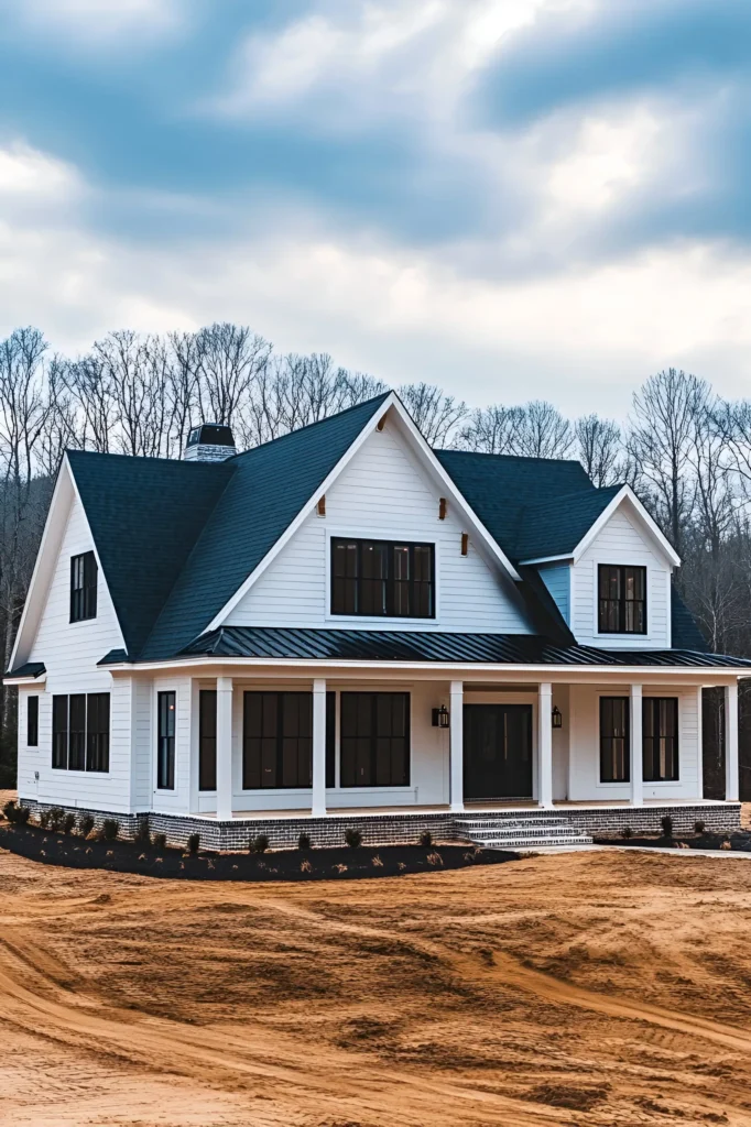 Modern white farmhouse with a black gabled roof, black-framed windows, and a wraparound porch, set against a natural wooded background.