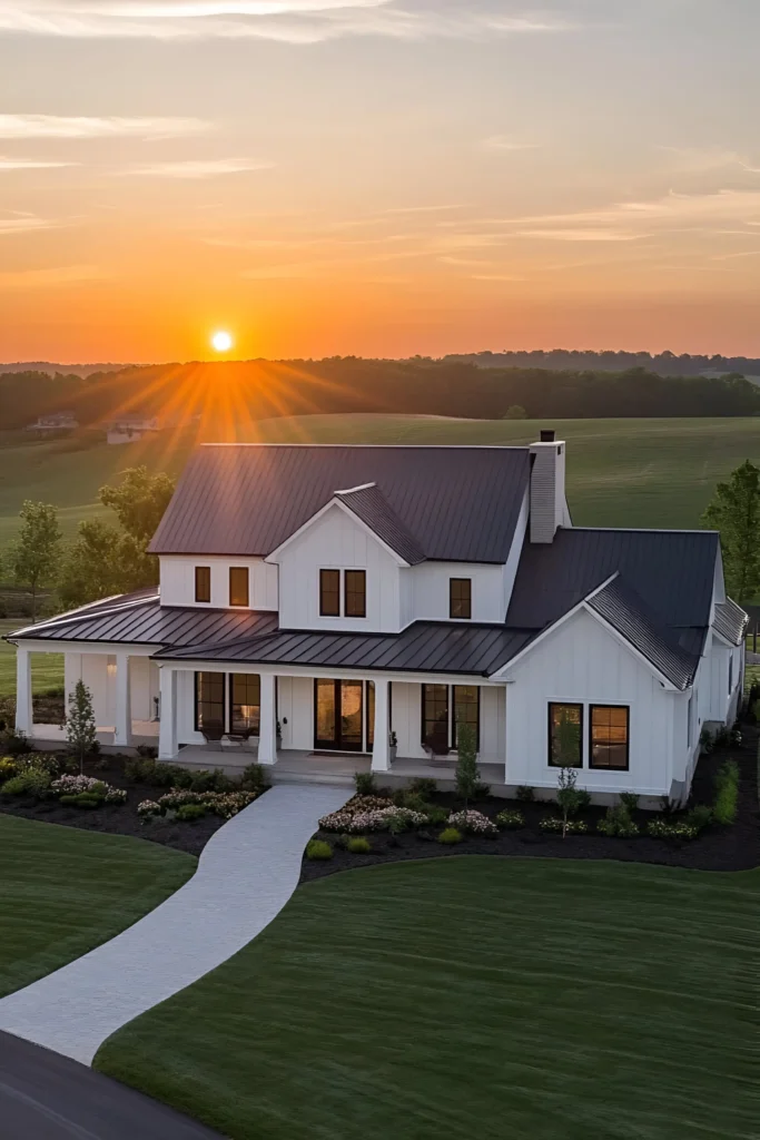 Modern white farmhouse with a black metal roof, landscaped gardens, and a sunset view over rolling fields.