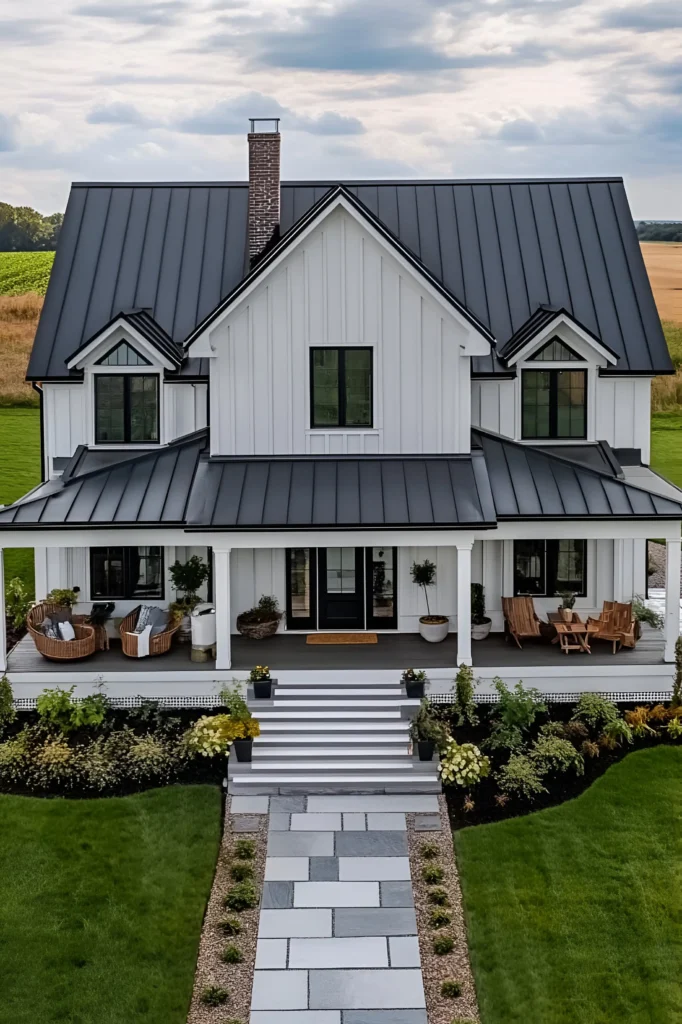 Modern white farmhouse with a black metal roof, wraparound porch with seating, stone pathway, and lush landscaping.