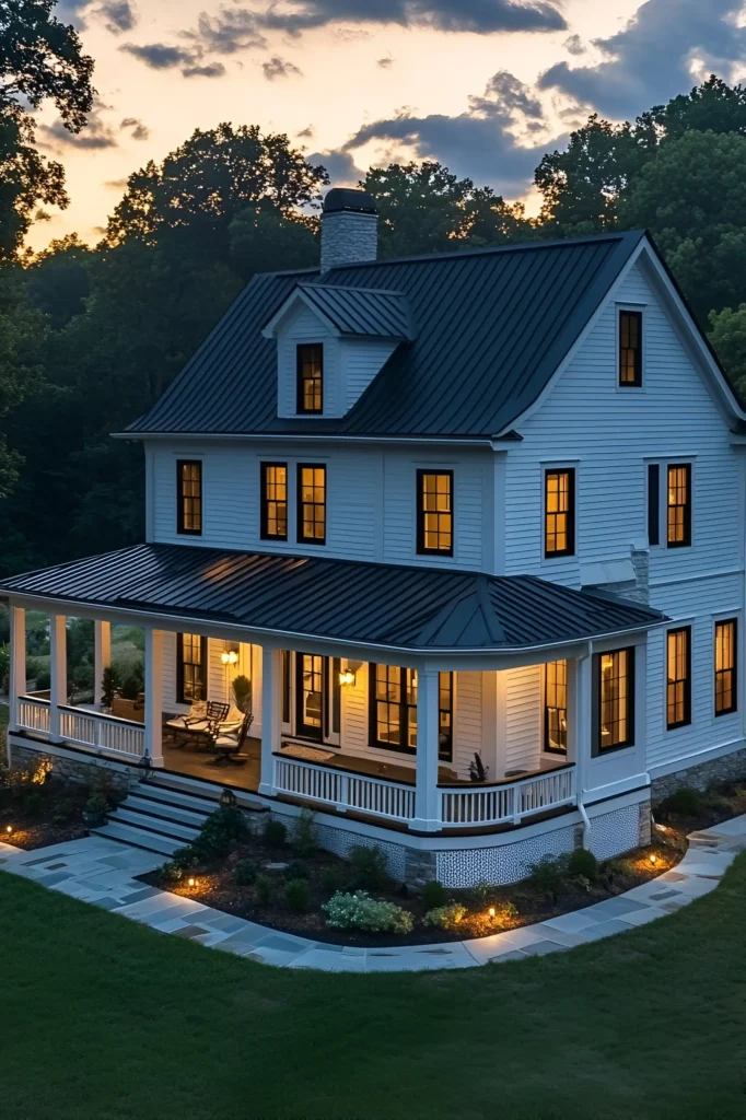 A glowing white farmhouse with a black metal roof and wraparound porch, featuring pathway lighting and lush landscaping under a twilight sky.