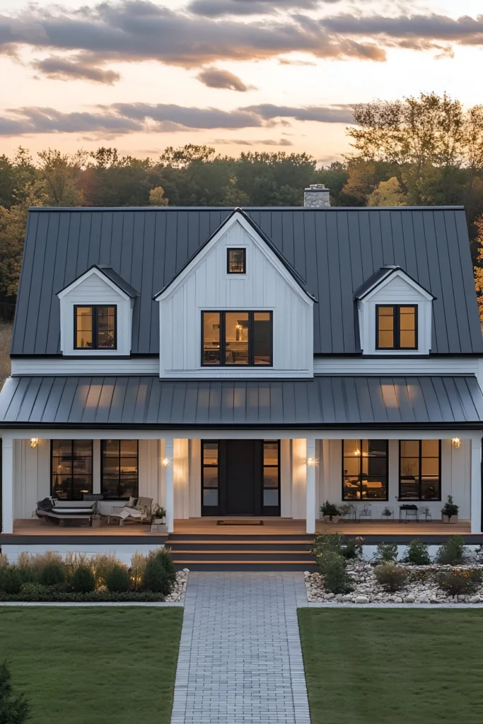 Modern white farmhouse with dormer windows, a black metal roof, and a cozy front porch illuminated at dusk.