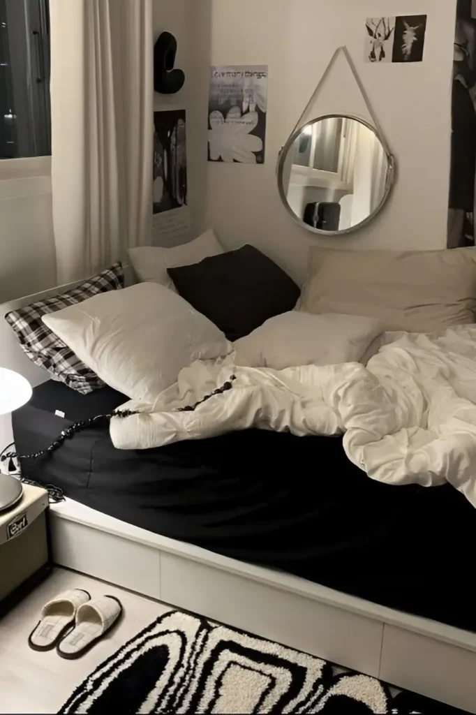 Small bedroom with black bedding, white decor, hanging round mirror, and monochrome modern accents.