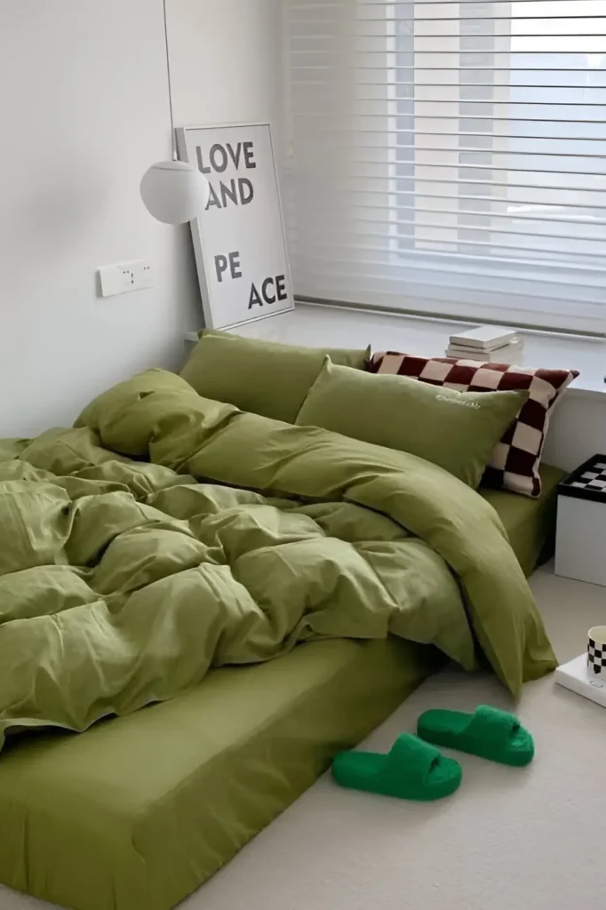 Small bedroom with olive green bedding, checkerboard accents, low bed design, and minimalist decor.