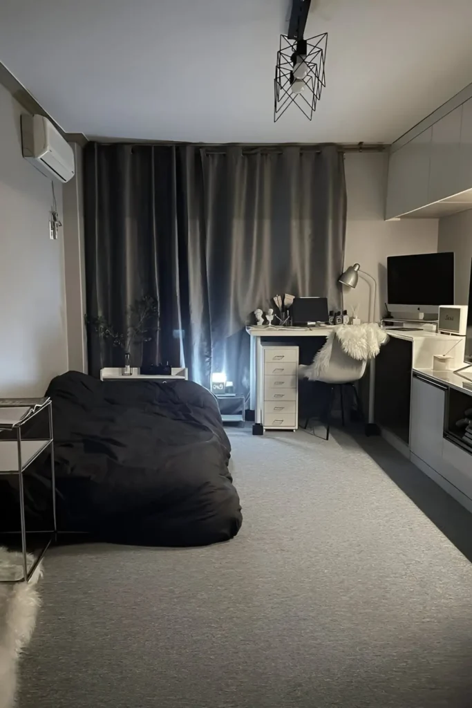 Modern small bedroom with black bedding, dark curtains, white workspace desk, and minimalist decor.