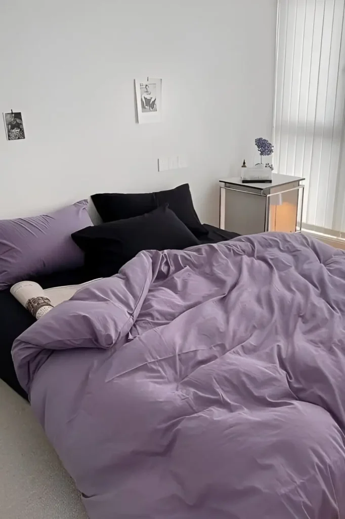 Small bedroom with soft purple bedding, black pillows, mirrored side table, and minimalist decor