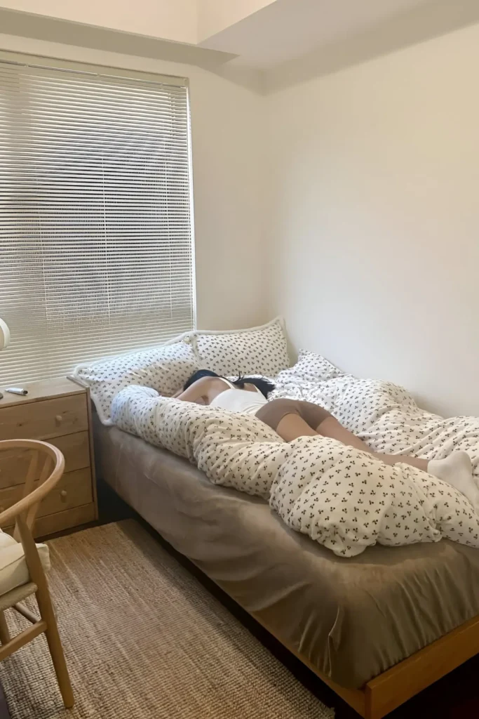 Minimal small bedroom with wooden furniture, patterned bedding, woven rug, and soft natural light.