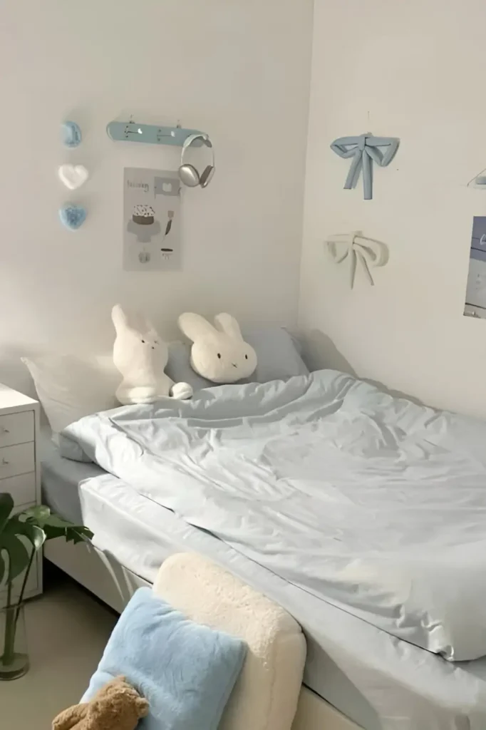 Soft pastel bedroom with light blue bedding, plush bunny toys, and minimal wall decorations.