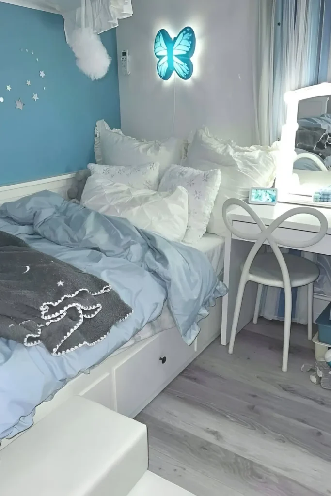 Blue-themed bedroom with butterfly wall light, cozy bedding, and white vanity setup.