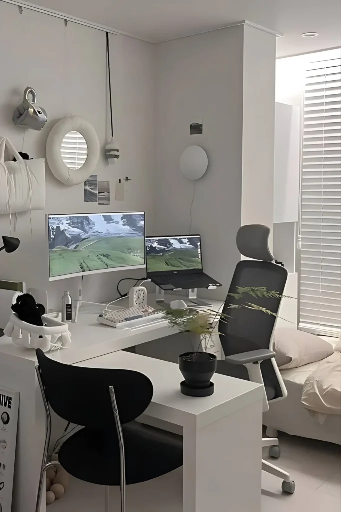 Minimalist dual monitor desk setup with an ergonomic chair, clean white desk, wall-mounted decor, and greenery for a functional and calming workspace.