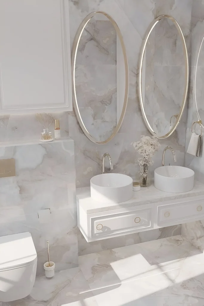 Chic white bathroom featuring marble walls, oval gold-framed mirrors, a floating double vanity, vessel sinks, and gold hardware.