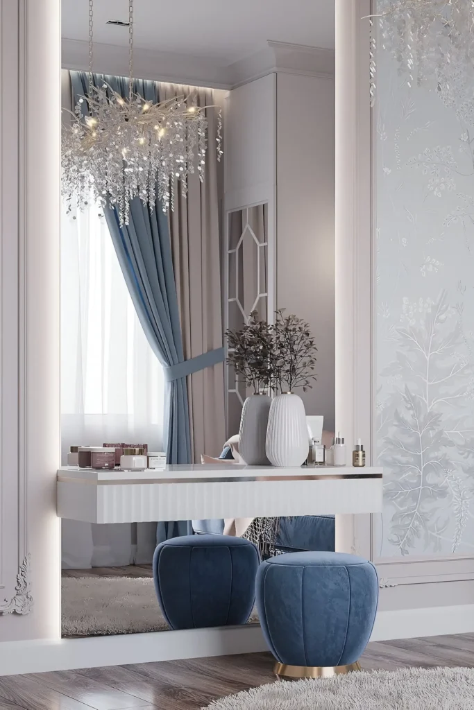 Glamorous white vanity with illuminated mirror, plush blue ottomans, gold accents, delicate chandeliers, and soft drapery.