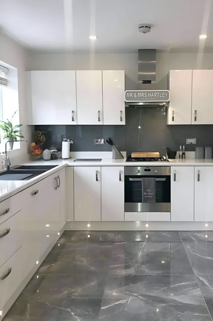 Modern kitchen with white cabinetry, gray backsplash, and reflective gray tile flooring.