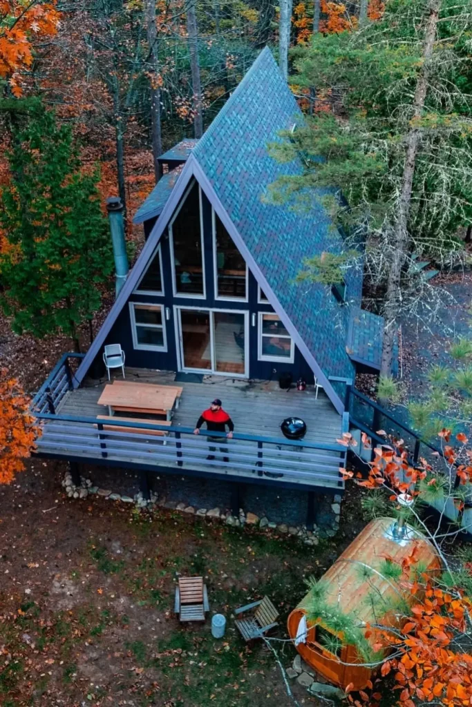 A-frame cabin with a spacious deck featuring a picnic table and grill, surrounded by vibrant autumn trees and a wood-fired sauna below.