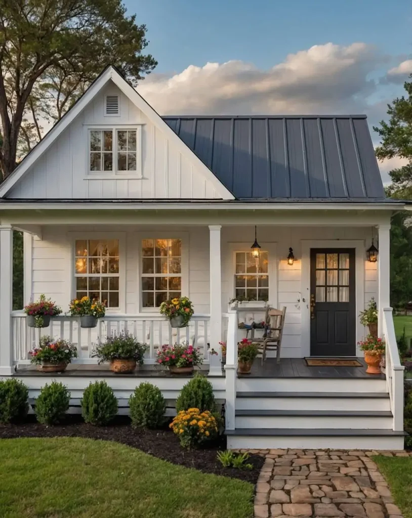 White cottage with a black door, flower-filled porch, and stone pathway.