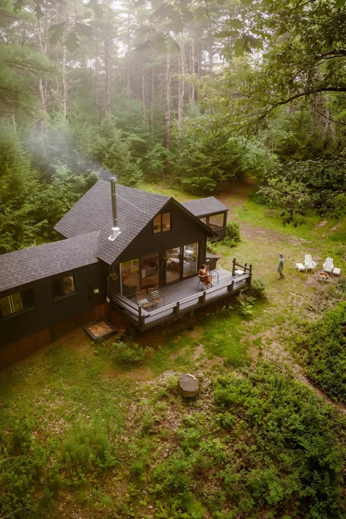 Modern secluded cabin with a deck and fire pit, surrounded by lush green forest.