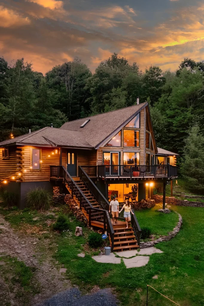 Rustic A-frame cabin with large glass windows, string lights, and elevated decks surrounded by greenery.