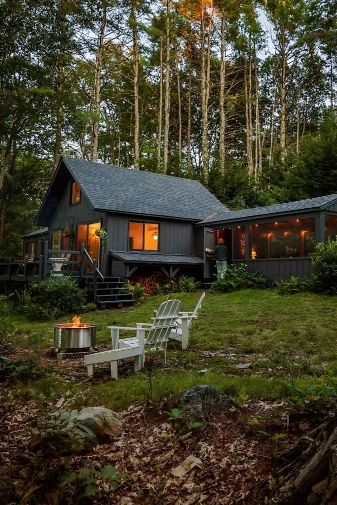 Modern cabin with screened porch, fire pit, and Adirondack chairs nestled in a lush forest.