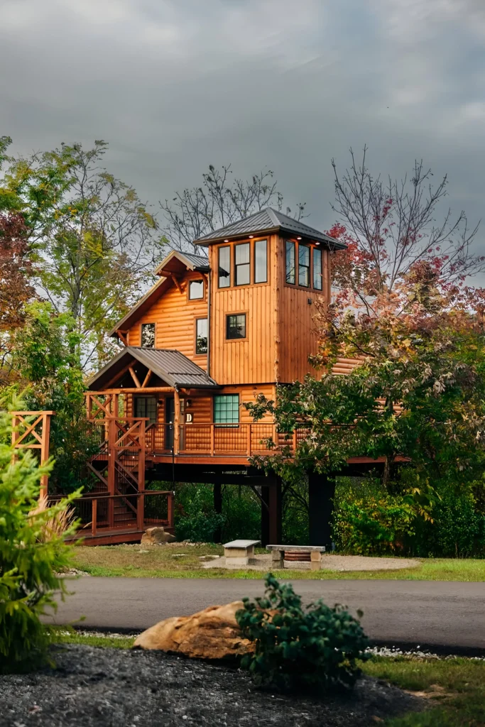 Rustic tower-style cabin with wood exterior, wraparound deck, and lush green surroundings.