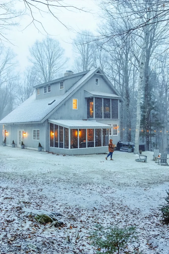 Cozy winter cabin with an enclosed porch, fire pit, and snow-covered surroundings in a forest setting.