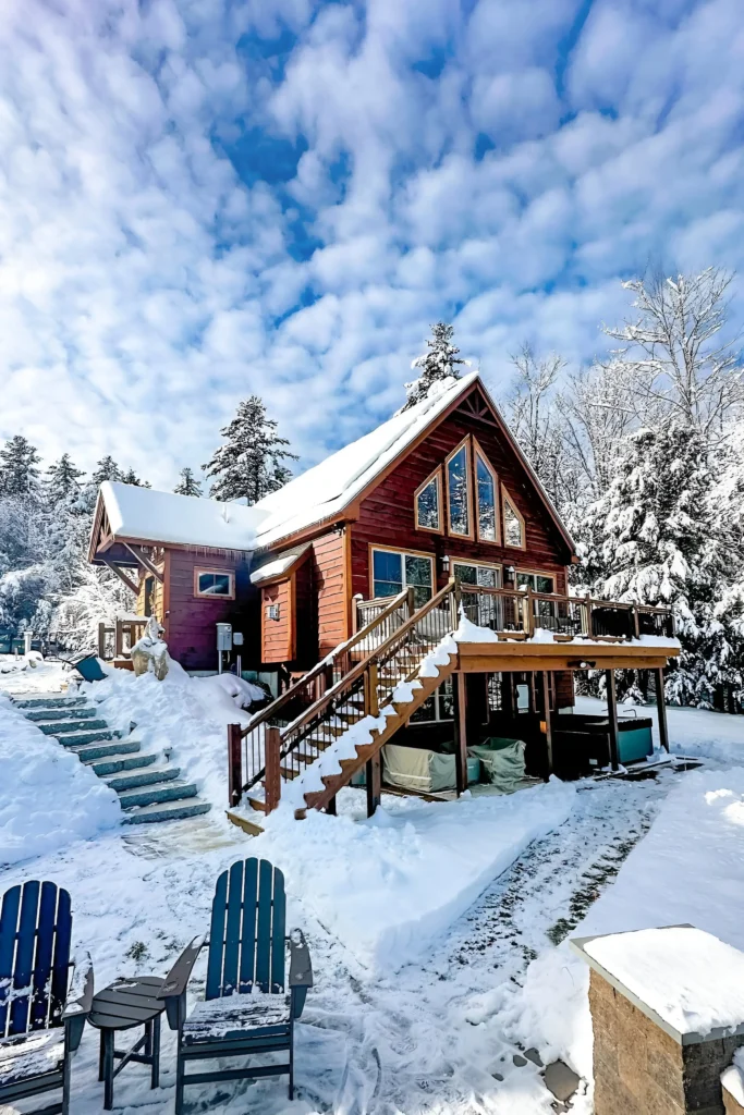 Snow-covered cabin with an elevated deck, fire pit, and bright blue winter sky backdrop.