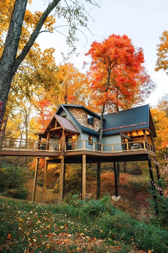 Elevated cabin surrounded by colorful autumn foliage, featuring a wraparound deck and rustic-modern design.