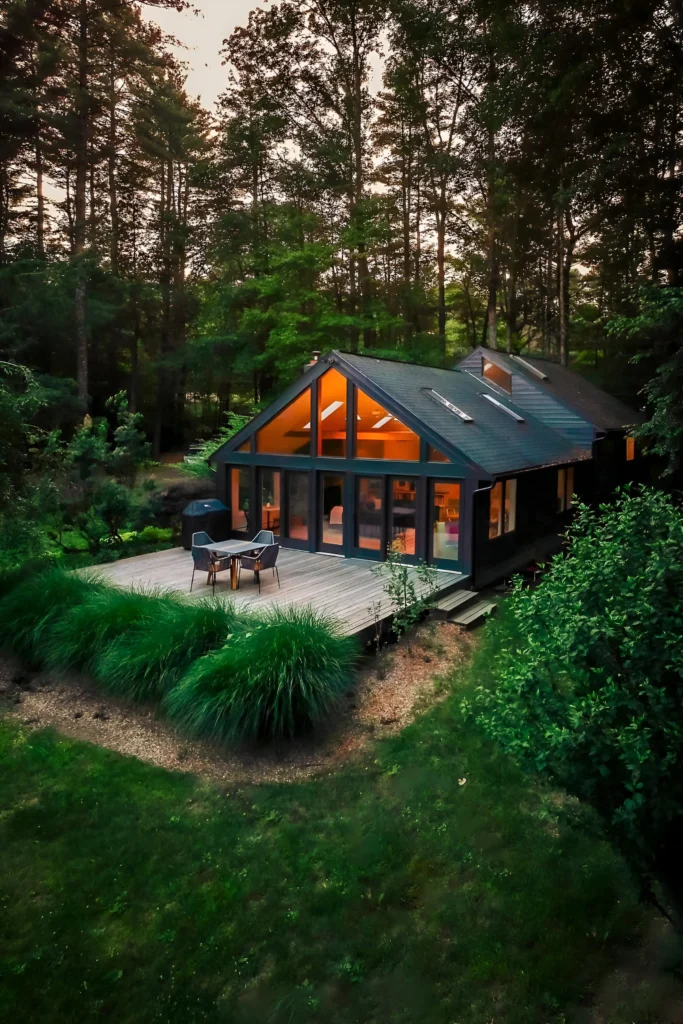 Modern forest cabin with floor-to-ceiling windows, a private deck, and lush green surroundings.