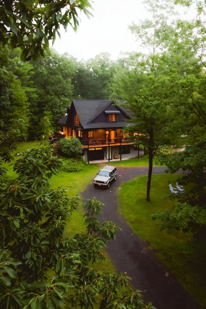 Secluded cabin with a wraparound porch, glowing interiors, and a lush green forest setting.