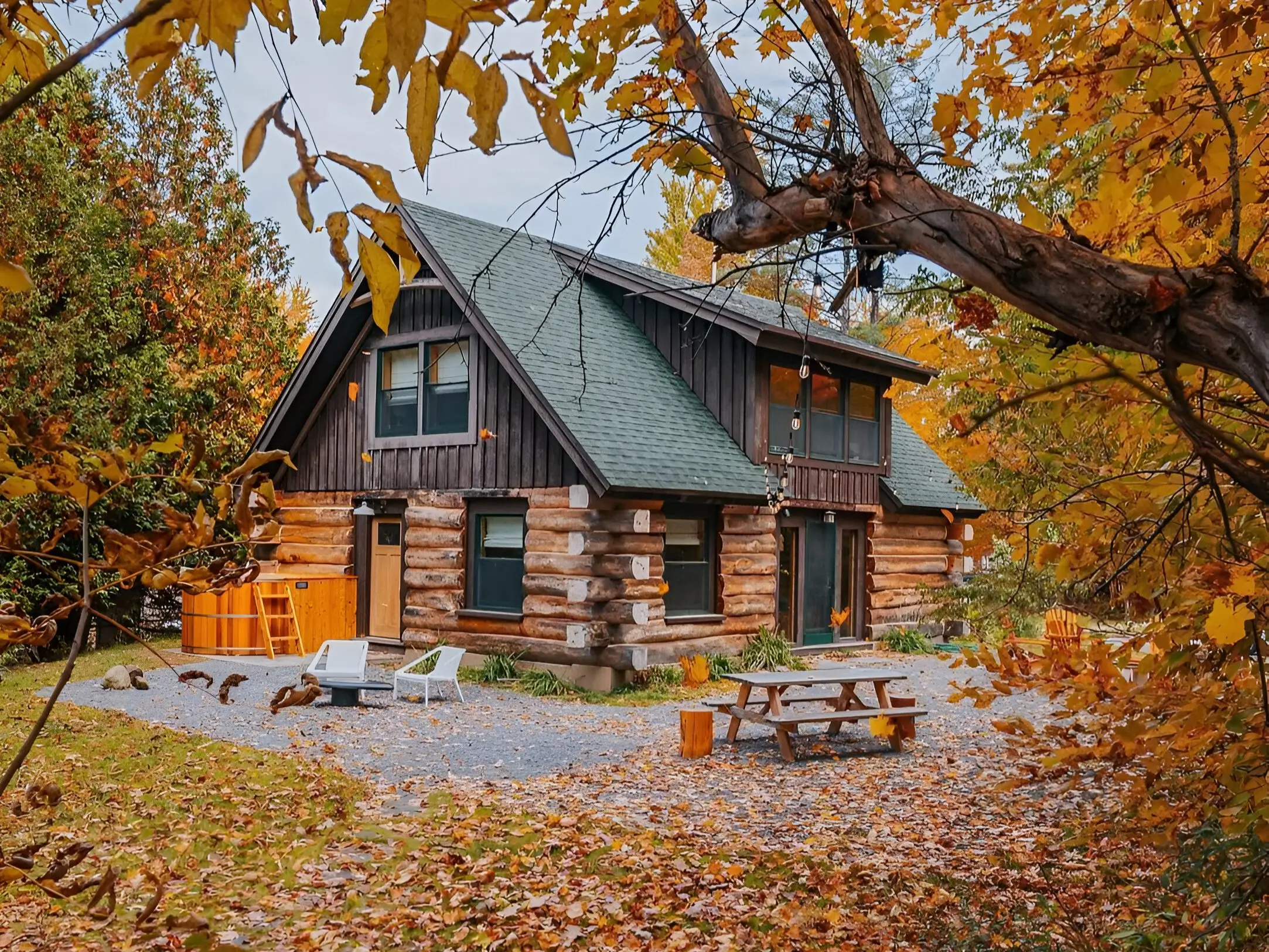 Rustic log cabin surrounded by colorful autumn leaves, featuring outdoor seating and a fire pit.