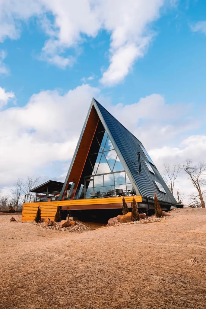 Modern A-frame house with a black metal roof, wood siding, large glass panels, and a spacious deck in an open landscape.