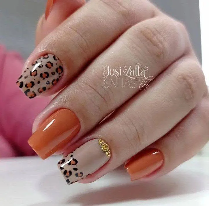 Orange nails with leopard print accents and gold stud details.