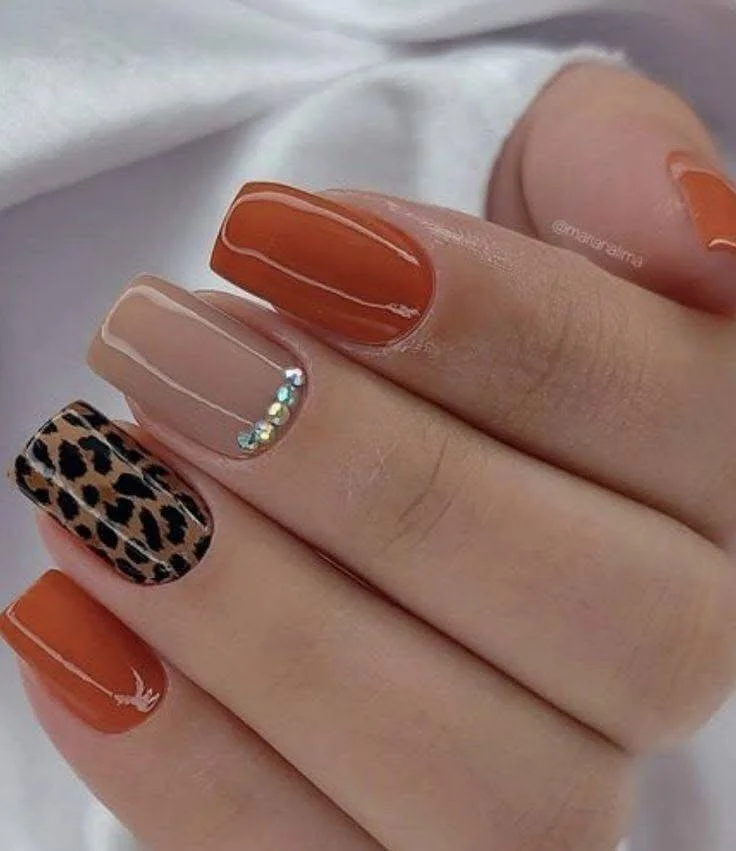 Burnt orange and nude nails with leopard print and crystal accents.