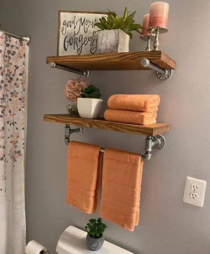 DIY industrial pipe shelving with wooden planks for bathroom towel storage.