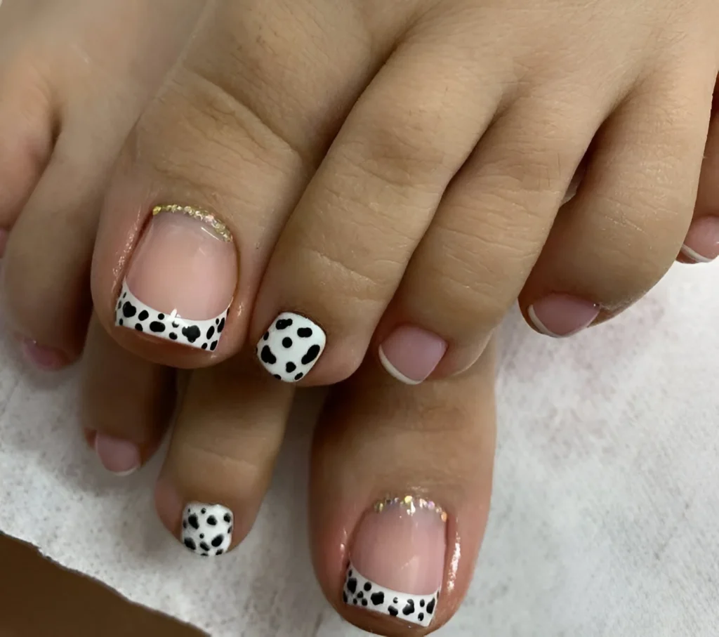 Dalmatian print French tip toenail design with gold glitter accents.