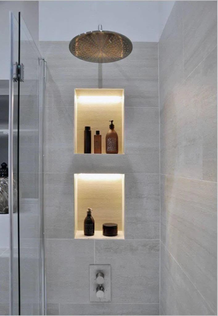 Modern bathroom with illuminated square wall niches and light gray tiles.