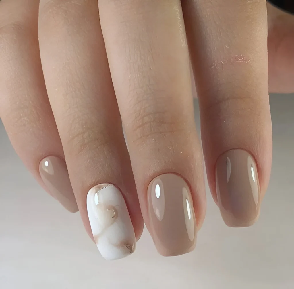 Beige nails with a glossy finish and a white and gold marble accent nail.