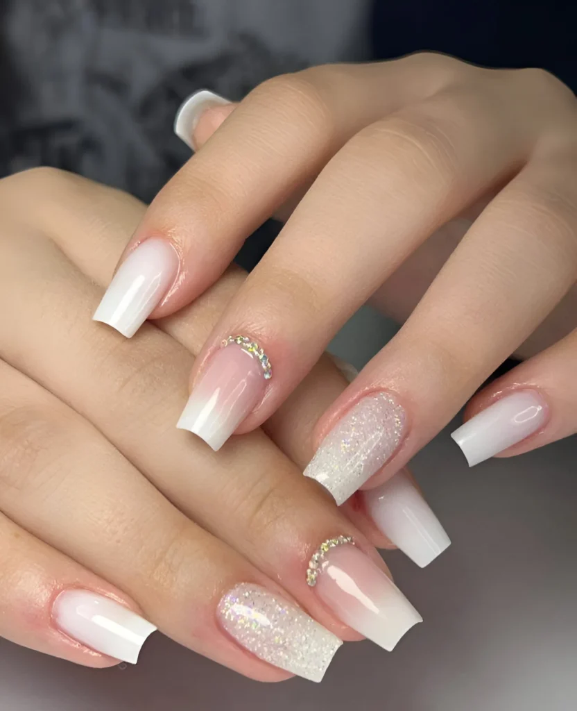 Baby boomer nails with crystal embellishments and a glitter accent nail on long, coffin-shaped nails.