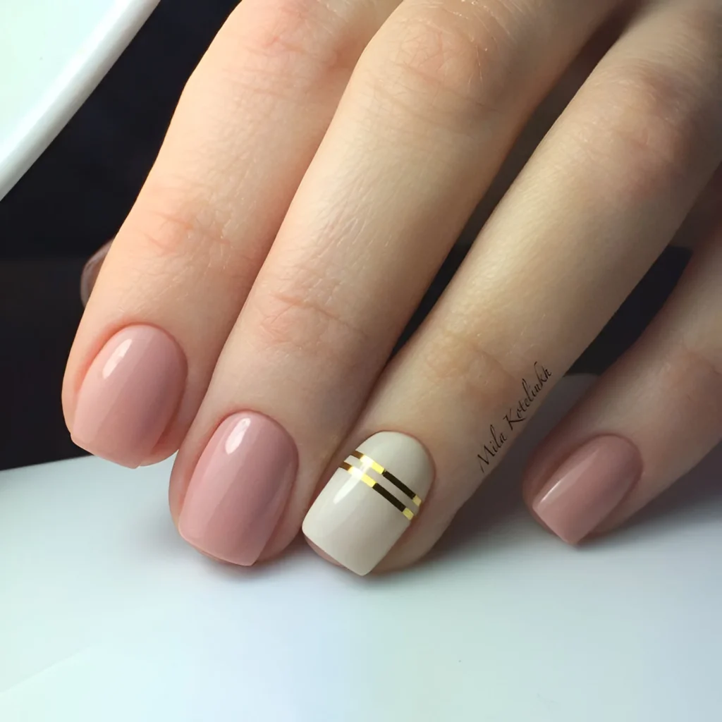 Nude-pink nails with a single accent nail featuring two parallel gold stripes.