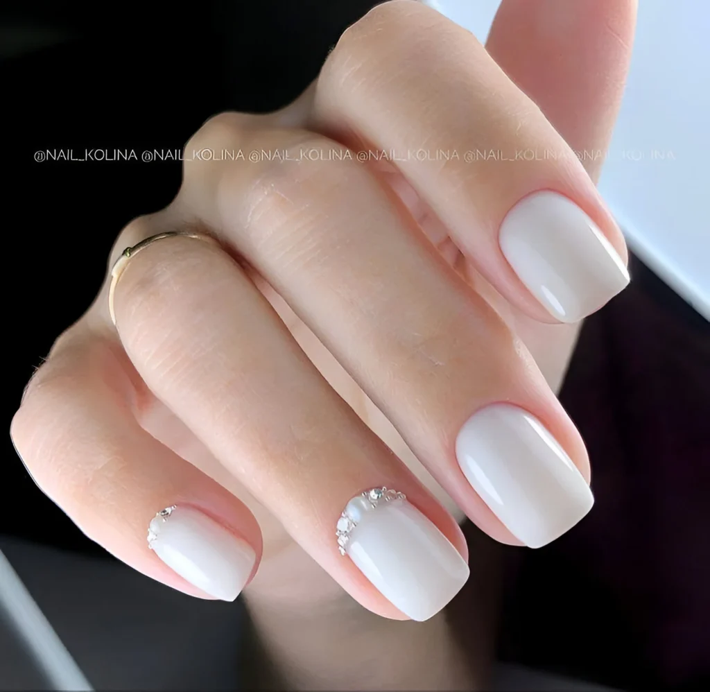 White nails with a glossy finish and crystal accents along the cuticle line.